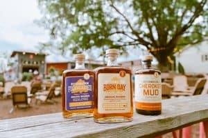 Reformation Brewery bourbon bottles on outdoor table with trees and seating in background.
